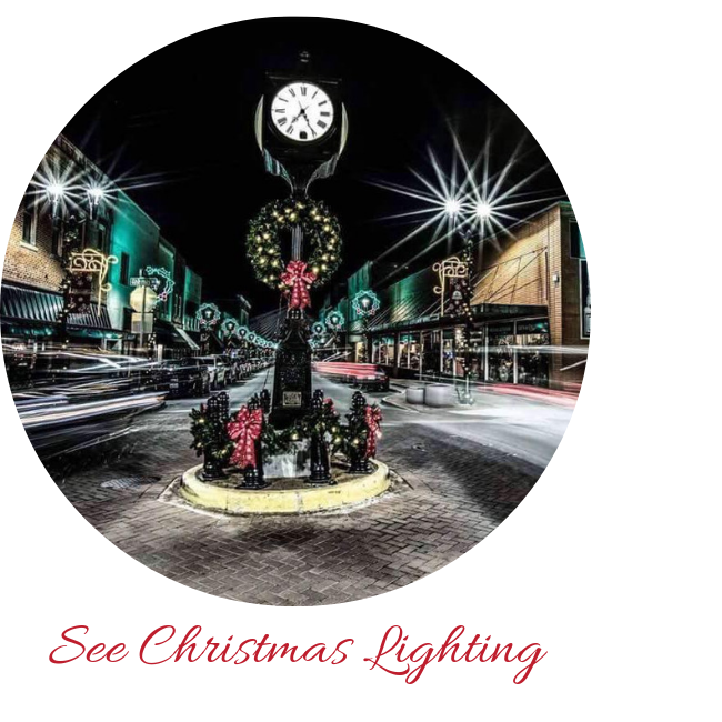 A festive downtown street at night featuring a central clock tower adorned with Christmas wreaths and red bows.