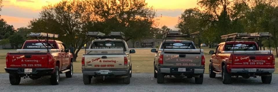 Four pickup trucks with ladder racks parked in a row outdoors at sunset.
