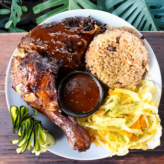 A plate of food with jerk chicken, rice and vegetables on a table