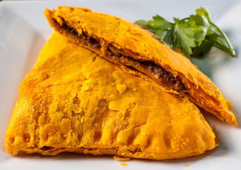 A close up of two jamaican beef patty on a white plate.