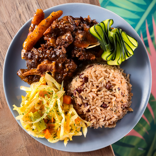 A plate of food with oxtail , rice and vegetables on a table
