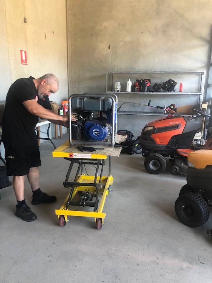 Man working on a generator on a yellow cart in a workshop with shelves and equipment — Cairns Small Engine Repairs in Bentley Park, QLD