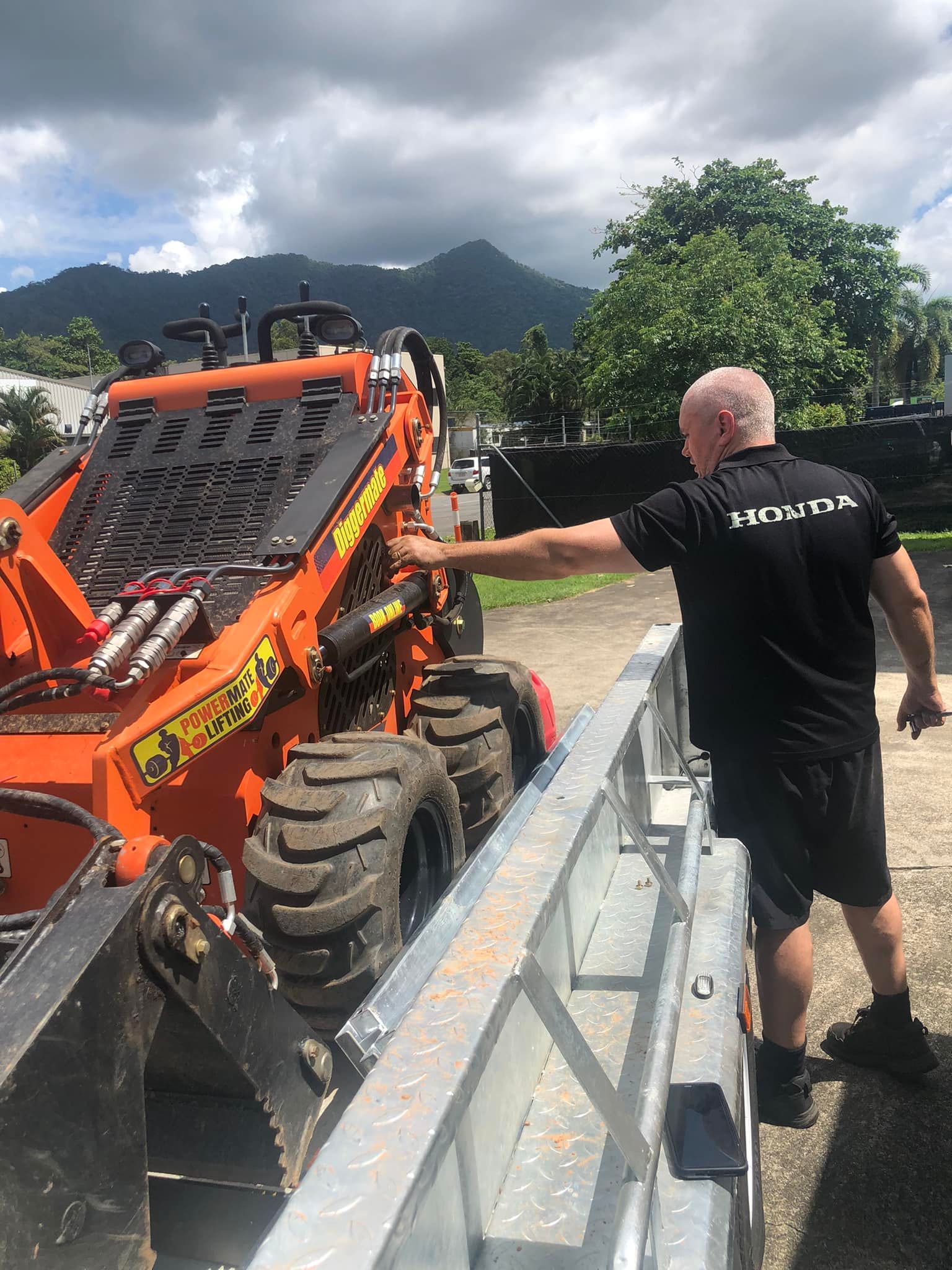 Man in black shirt loading orange off-road vehicle onto a trailer with mountains in the background — Cairns Small Engine Repairs in Bentley Park, QLD