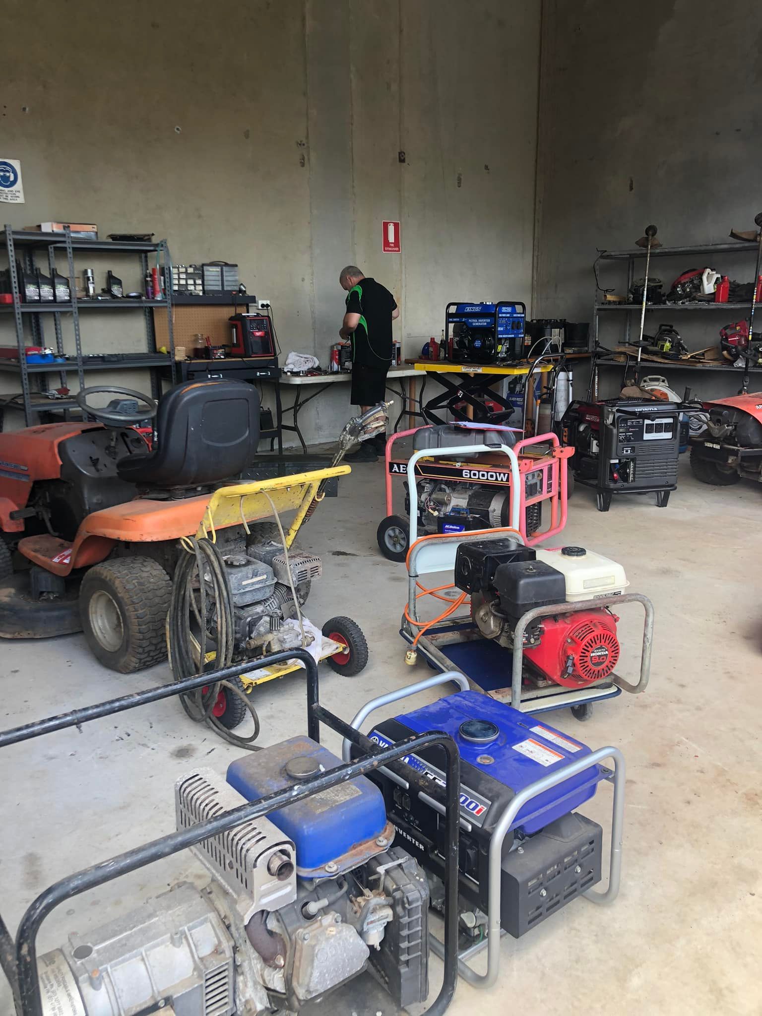 Garage workshop with several portable generators and equipment on the floor, shelves of tools in the background — Cairns Small Engine Repairs in Bentley Park, QLD