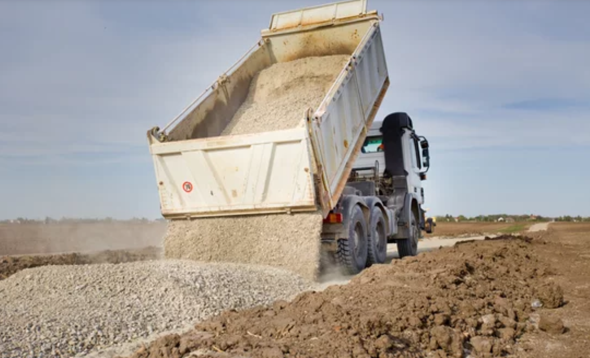 Large truck dumping a load of gravel onto a construction site.