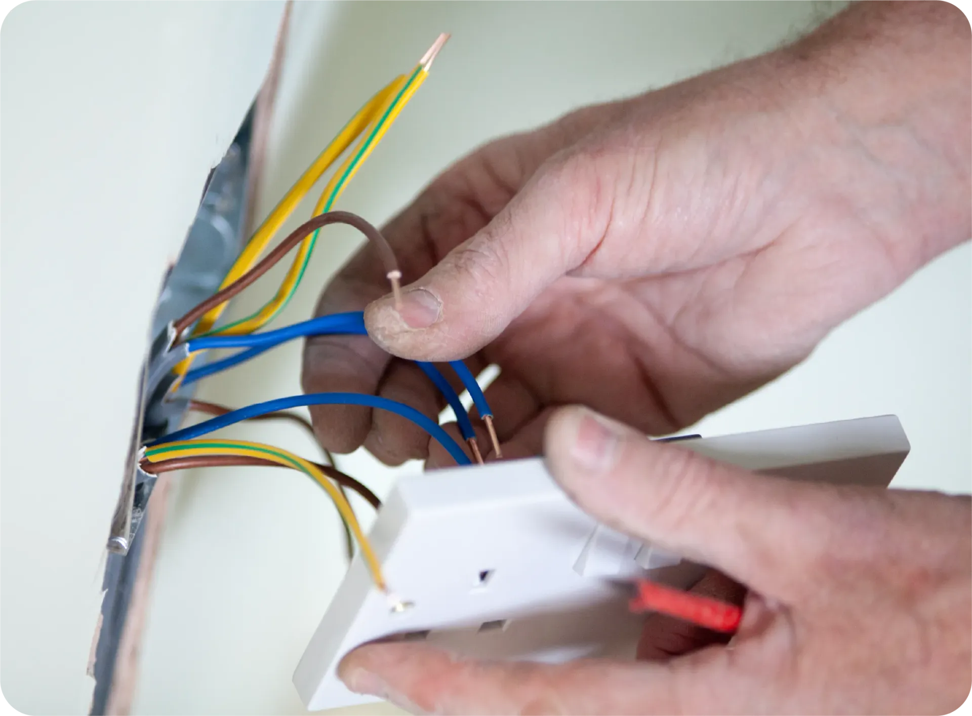 Hands of an electrician wiring a light switch, with visible colored wires and a wall outlet box.