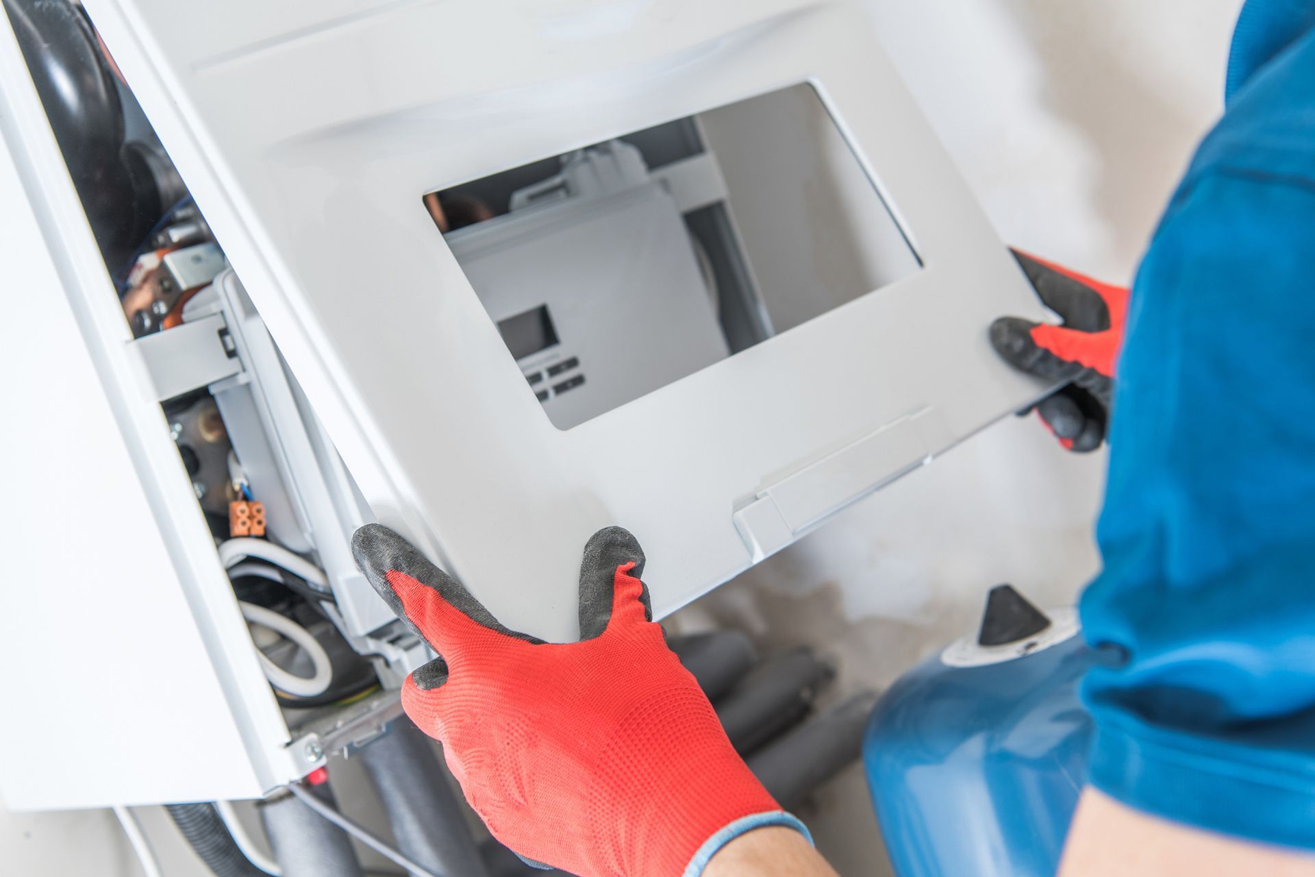 A man wearing red gloves is working on a boiler.