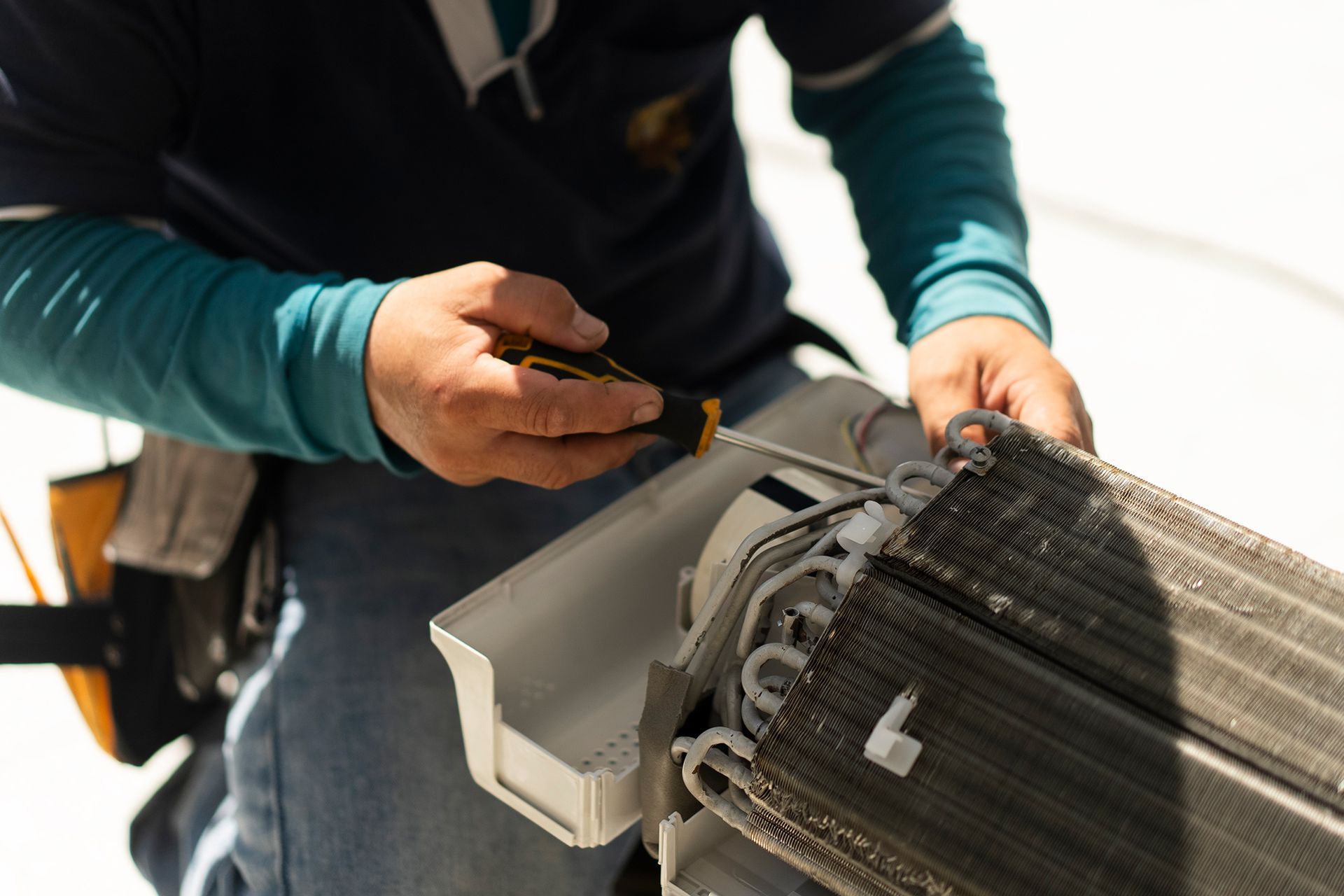 A man is fixing an air conditioner with a screwdriver.