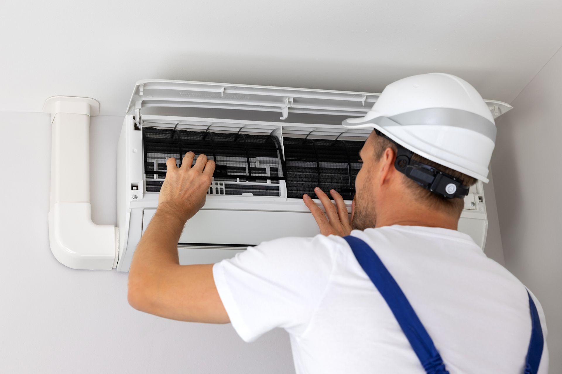 A man wearing a hard hat is working on an air conditioner.