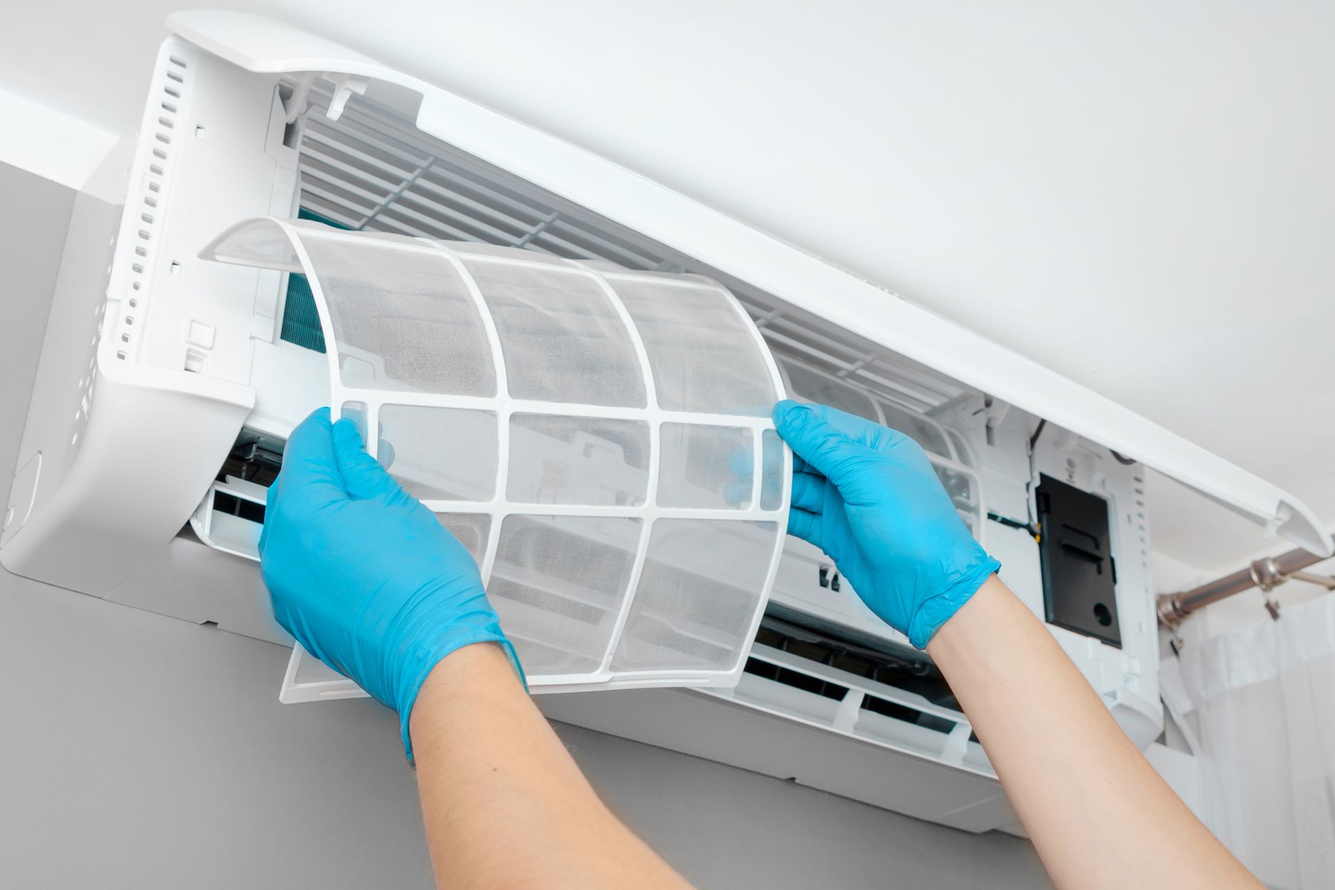 A person wearing blue gloves is cleaning an air conditioner.