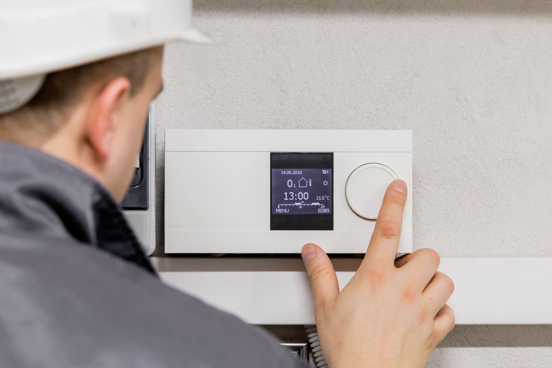 A man is adjusting a thermostat with his finger.