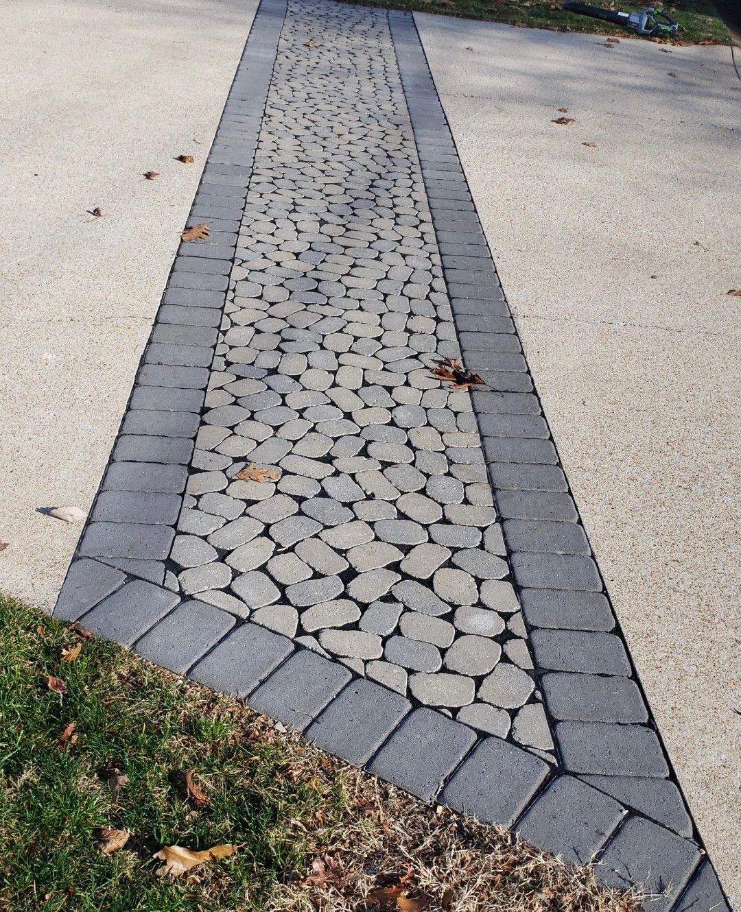 A brick walkway with a concrete border and grass on the side