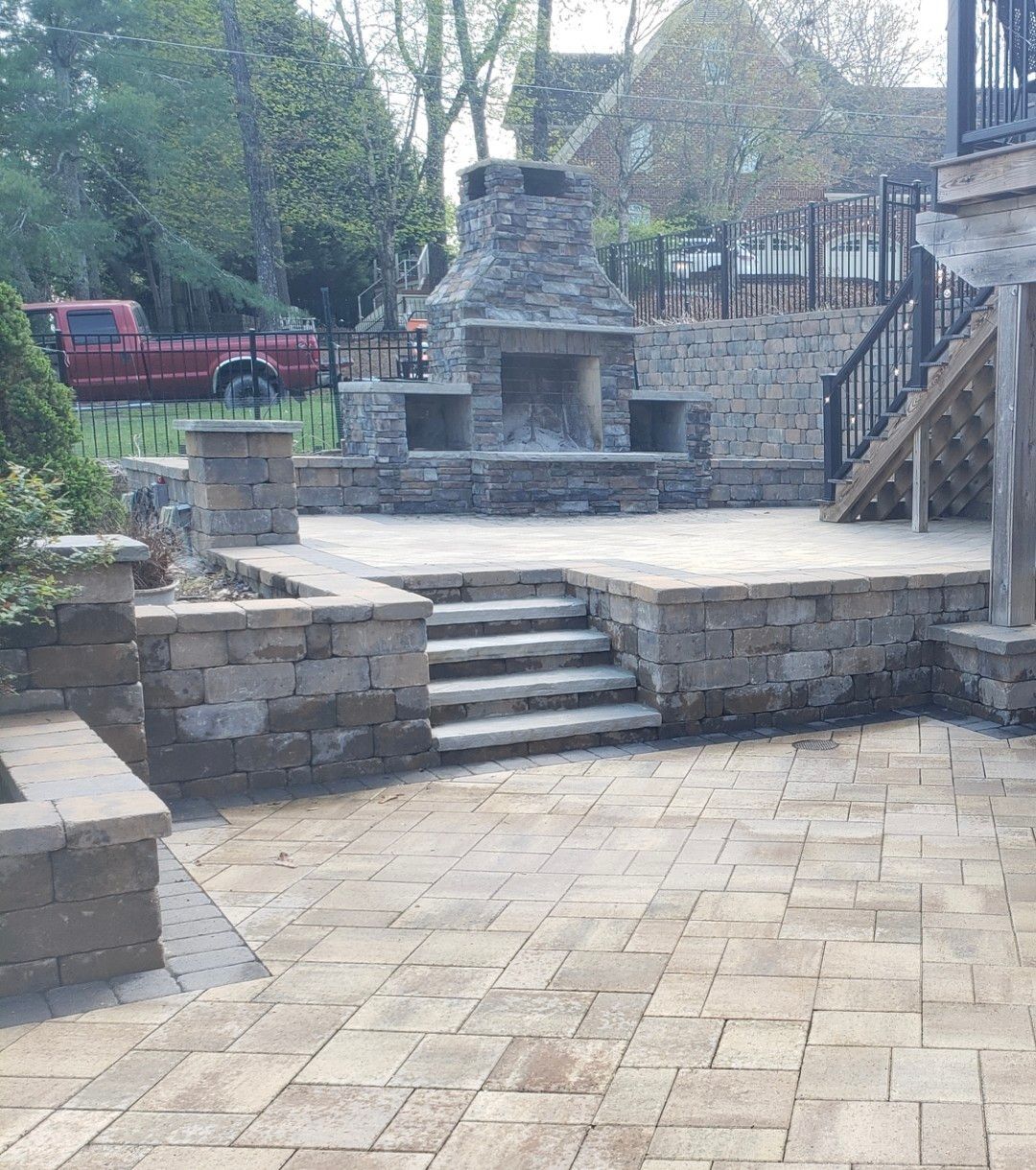 A brick patio with a stone fireplace and stairs