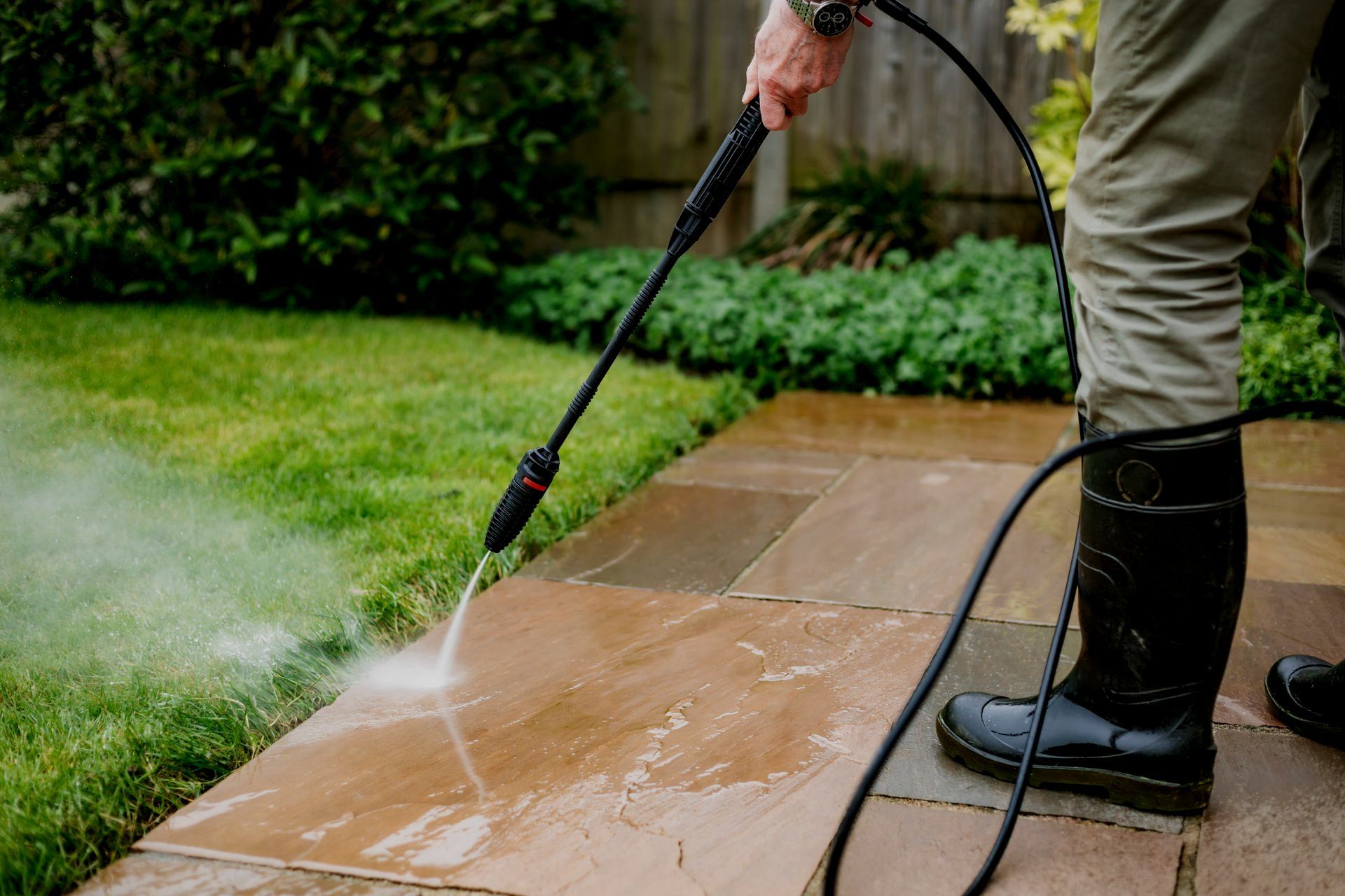 A man is using a high pressure washer to clean a patio.