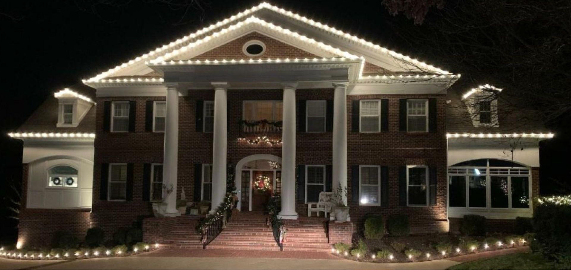 A large brick house is lit up with christmas lights at night.