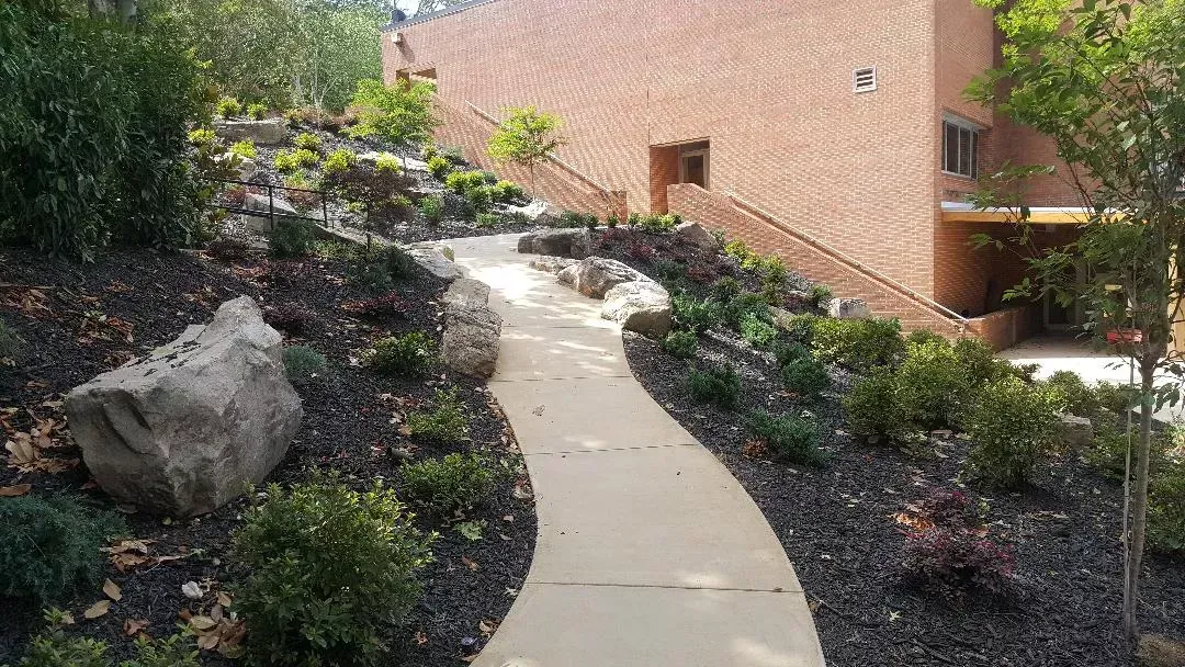 A walkway leading to a brick building surrounded by rocks and bushes.