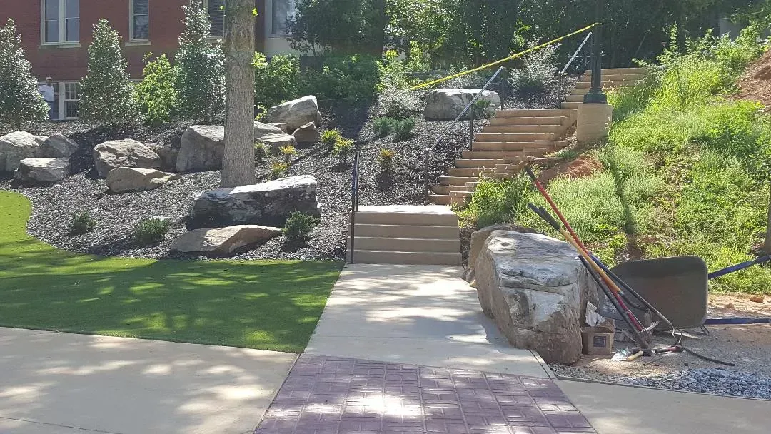 A concrete walkway leading to a staircase in a park with a wheelbarrow in the foreground.