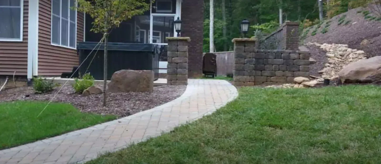 A brick walkway leading to a house with a screened in porch.