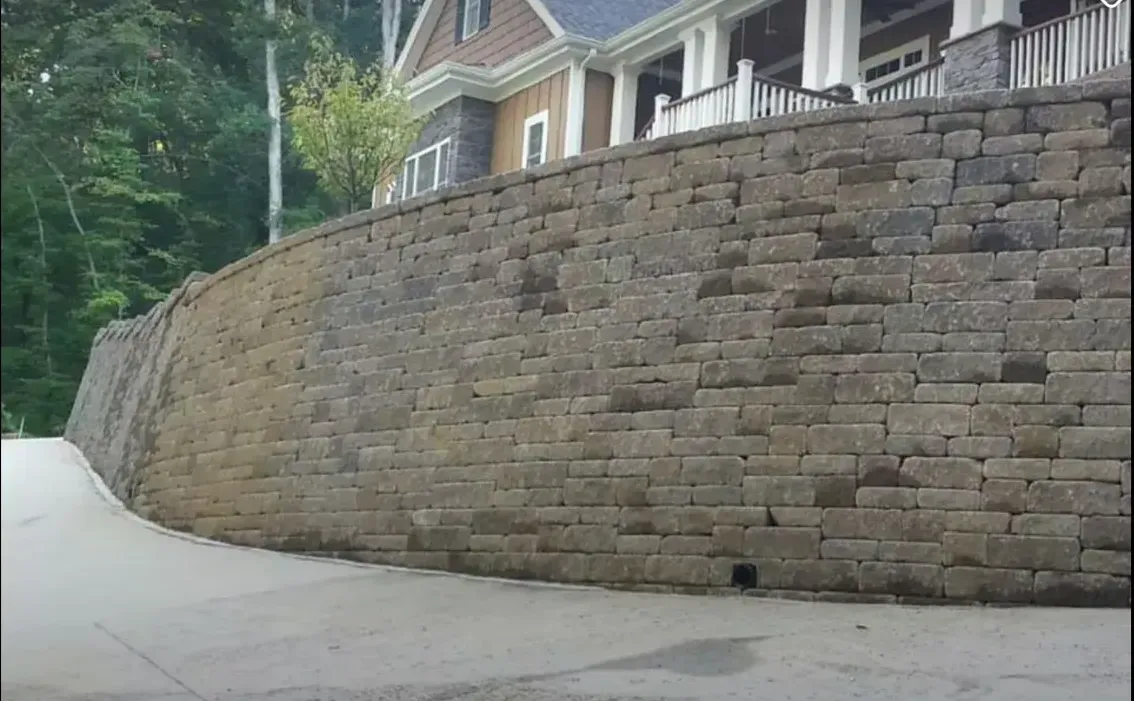 A large brick wall surrounds a curvy road in front of a house.