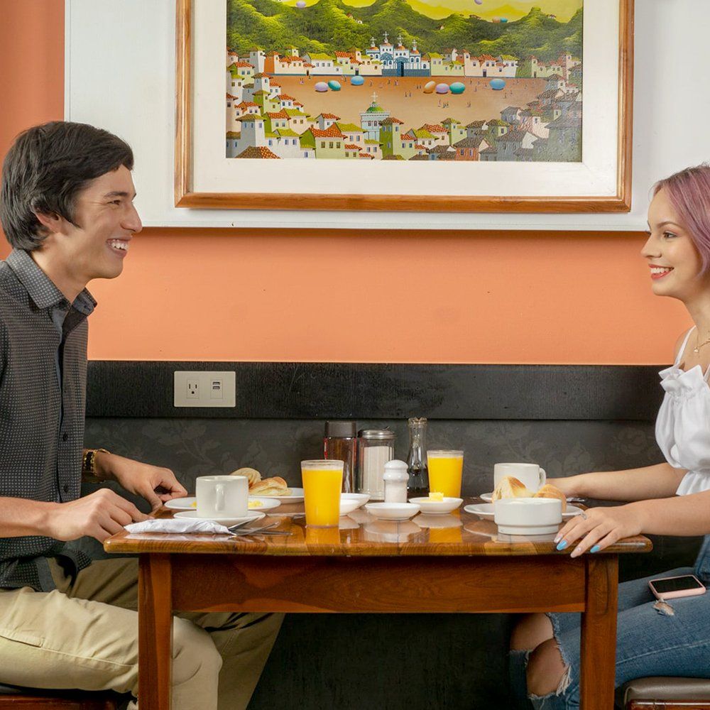 Un hombre y una mujer están sentados en una mesa con una imagen en la pared detrás de ellos