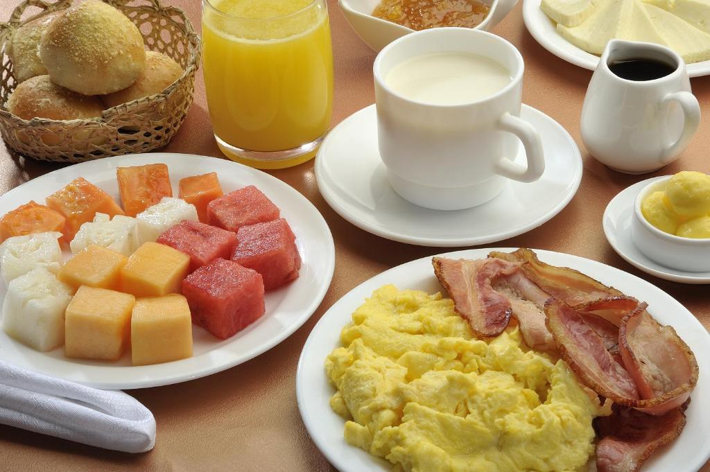 Una mesa con platos de comida que incluyen huevos revueltos, tocino y fruta.