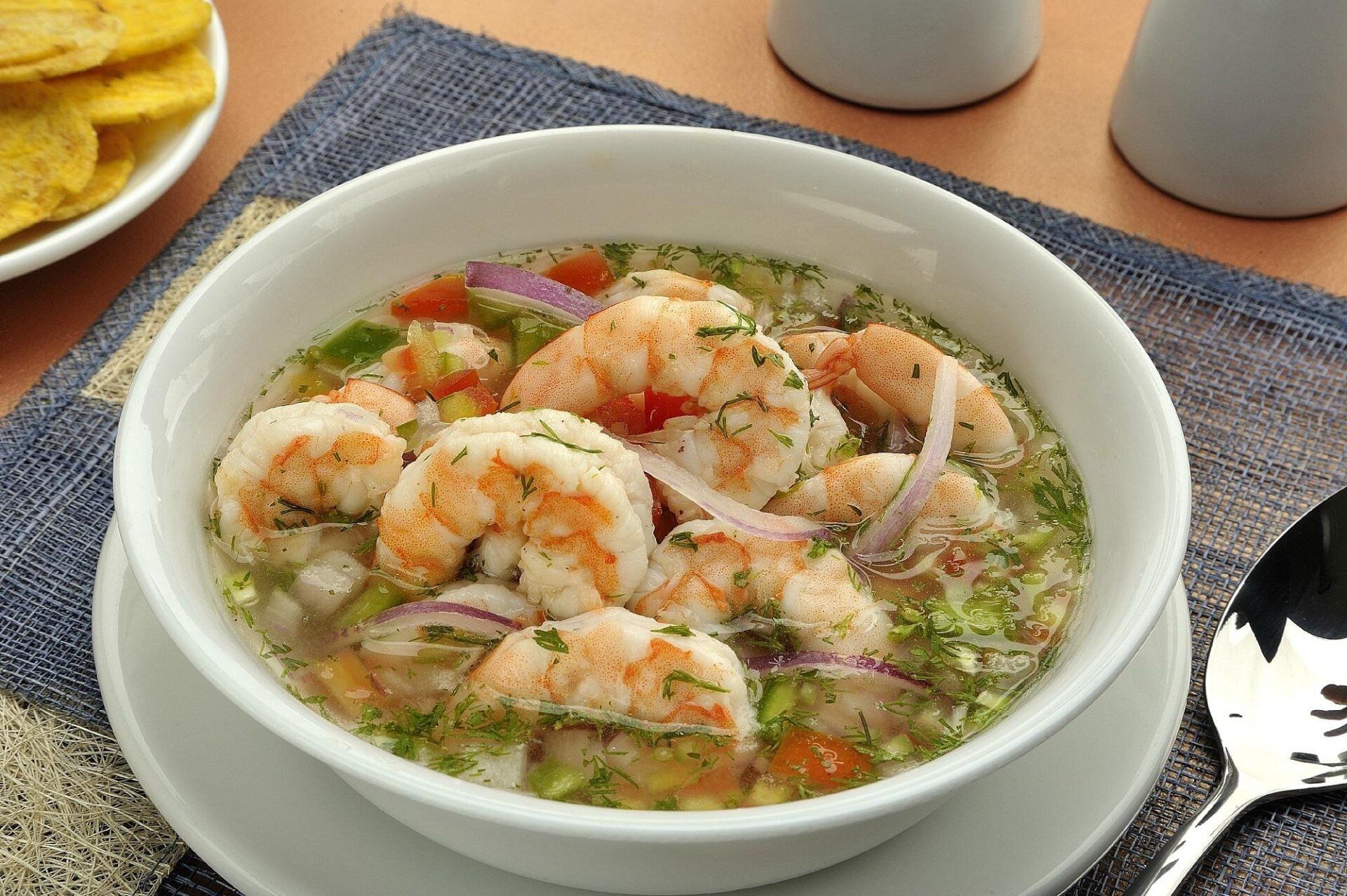 Un plato de sopa de camarones con una cuchara adentro.