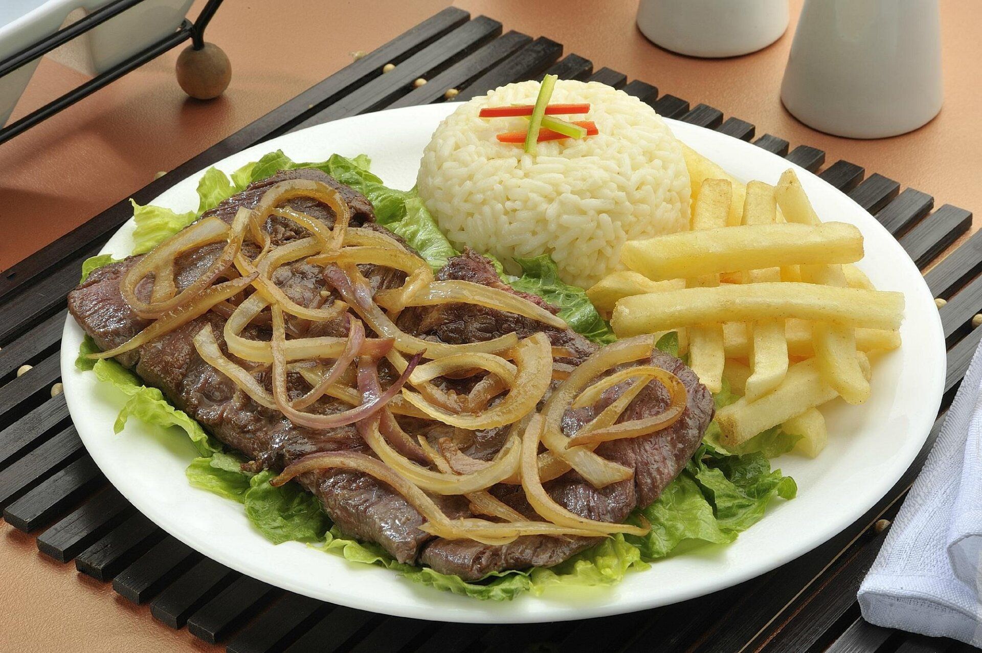 Un plato blanco con carne, arroz y papas fritas.