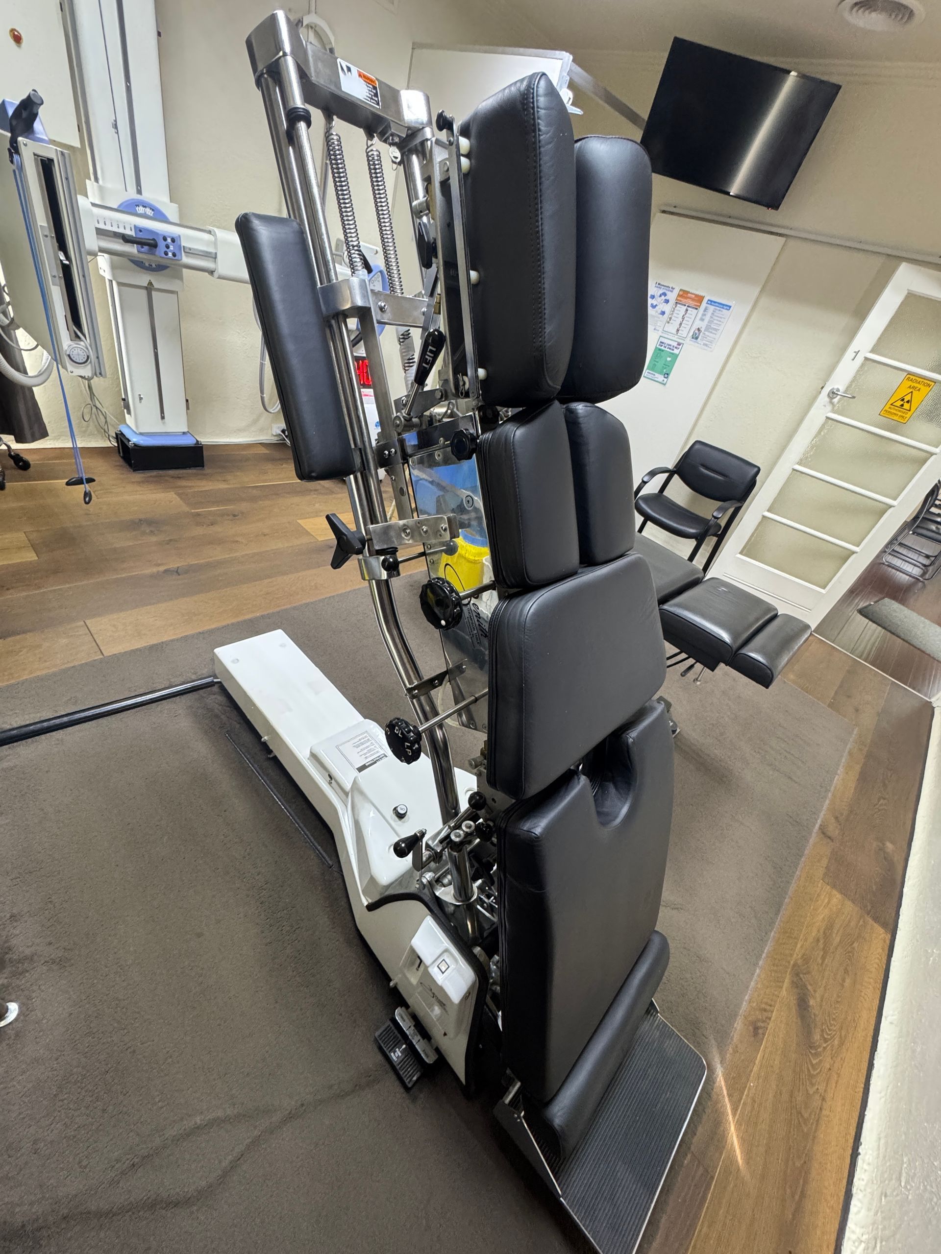 Chiropractic adjustment table in a doctor's office. The table is black and white, and has adjustable headrests and a leg rest.
