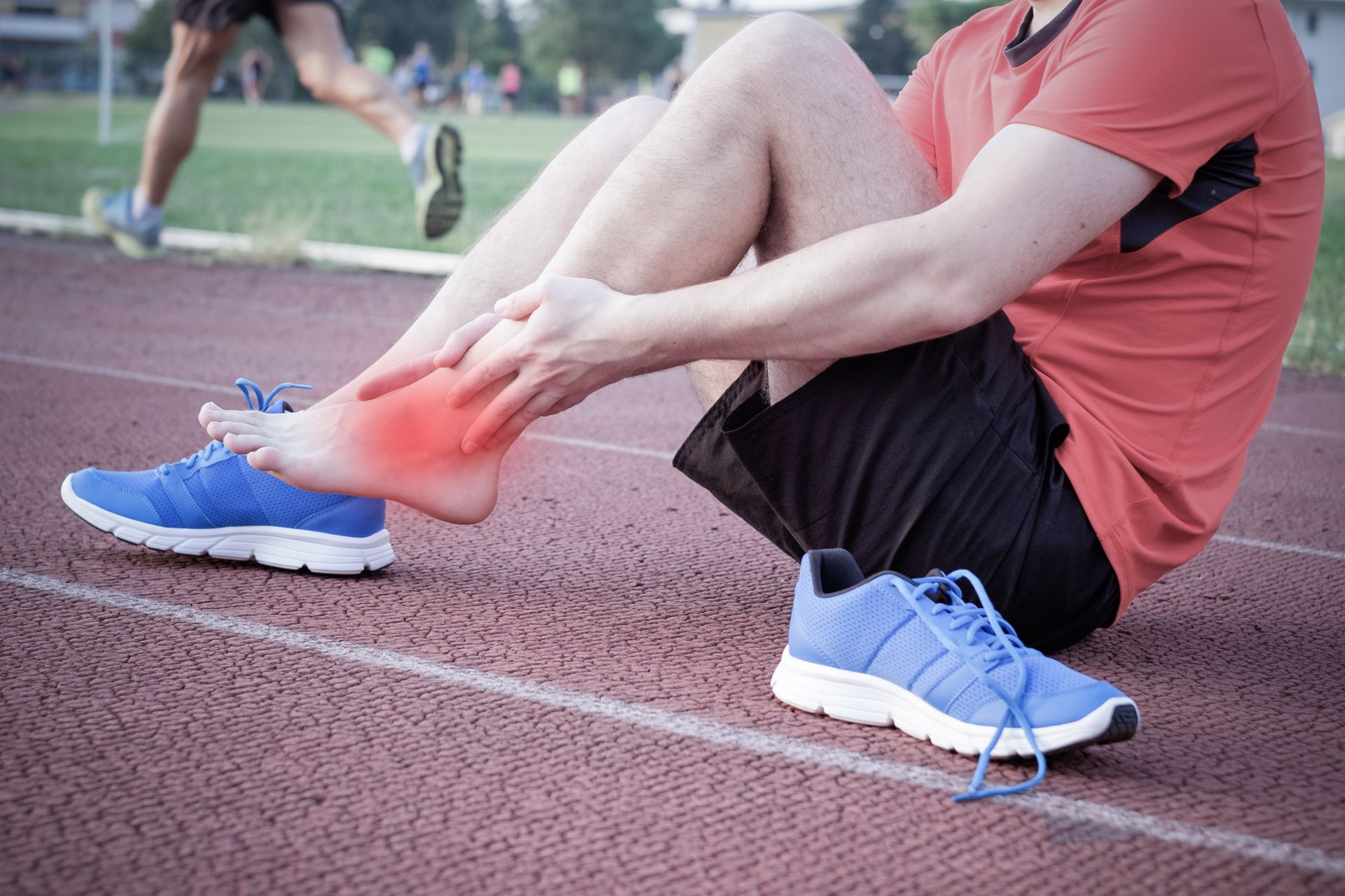 Runner on track with ankle injury, touching foot; red highlight indicates pain.