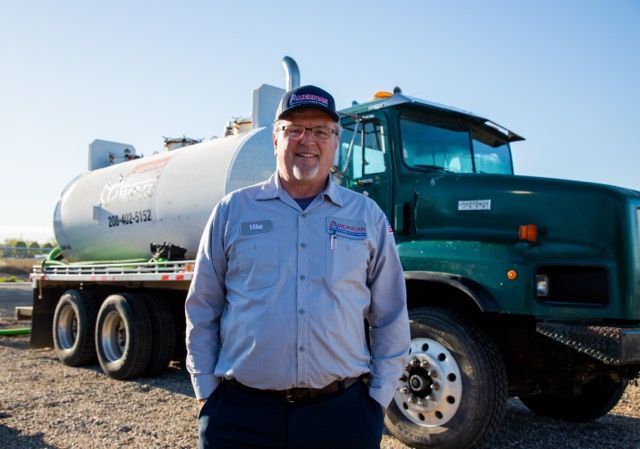 Septic pumping technician in front of large septic trunk.