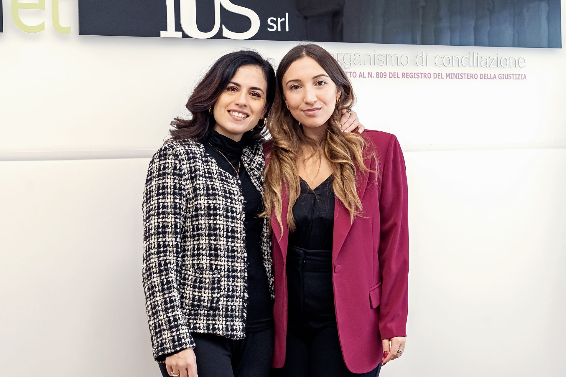 Due donne in posa: una con una giacca a fantasia bianca e nera, l'altra con un blazer rosso, entrambe abbracciate.