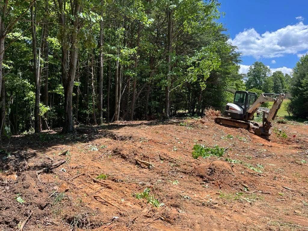 A bulldozer is sitting in the middle of a dirt field surrounded by trees.