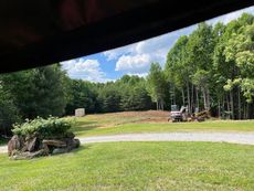A tractor is driving down a dirt road in a field surrounded by trees.