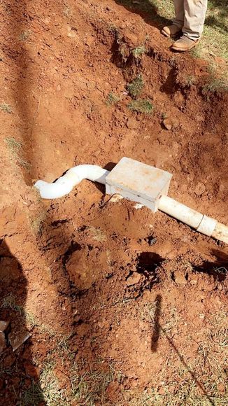 A person is standing next to a pipe in the dirt.