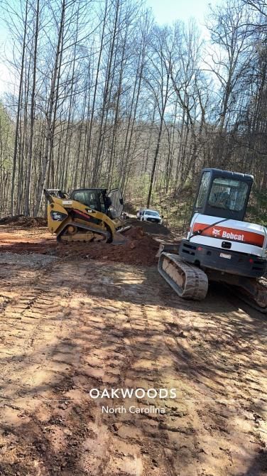 A bulldozer and a tractor are working on a dirt road in the woods.