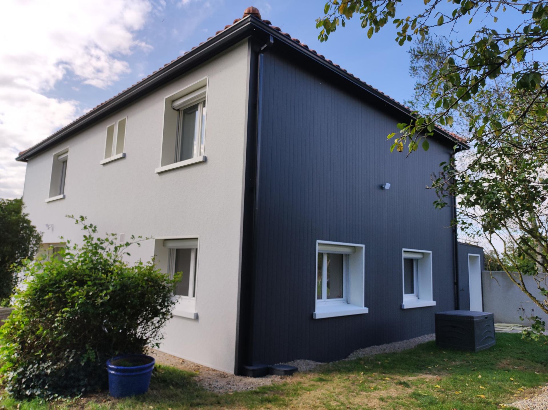 Une maison noire et blanche avec un pot bleu devant.