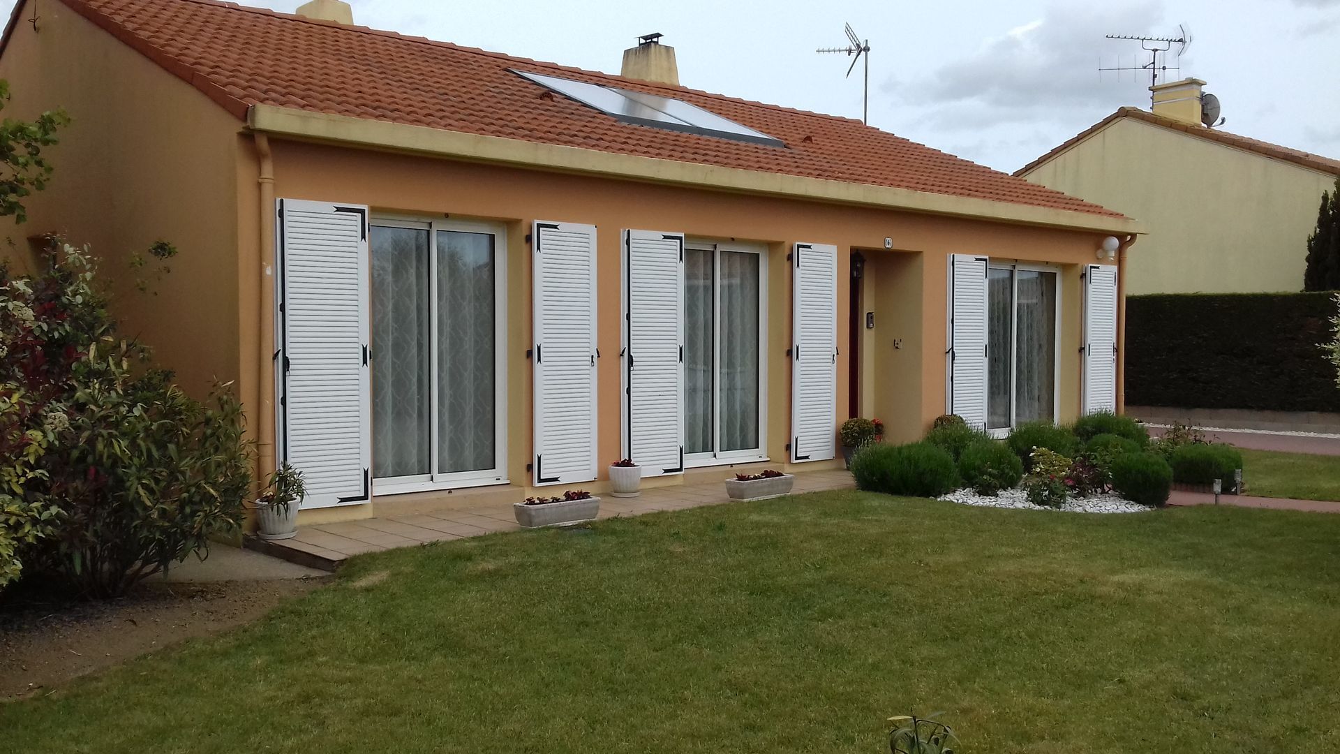 Une maison avec un toit de tuiles rouges et des volets blancs