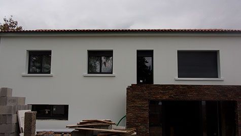 Une maison blanche avec trois fenêtres et un mur de briques est en construction.