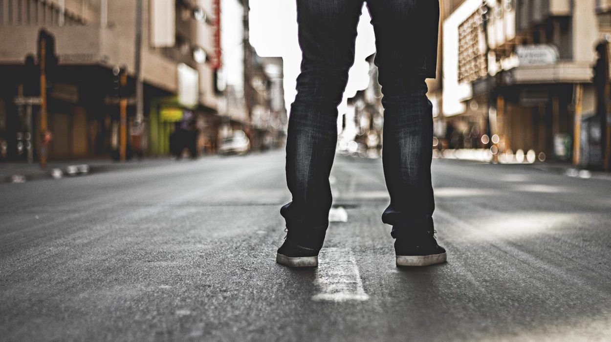 Person standing on a city street, legs apart, wearing dark jeans and shoes.