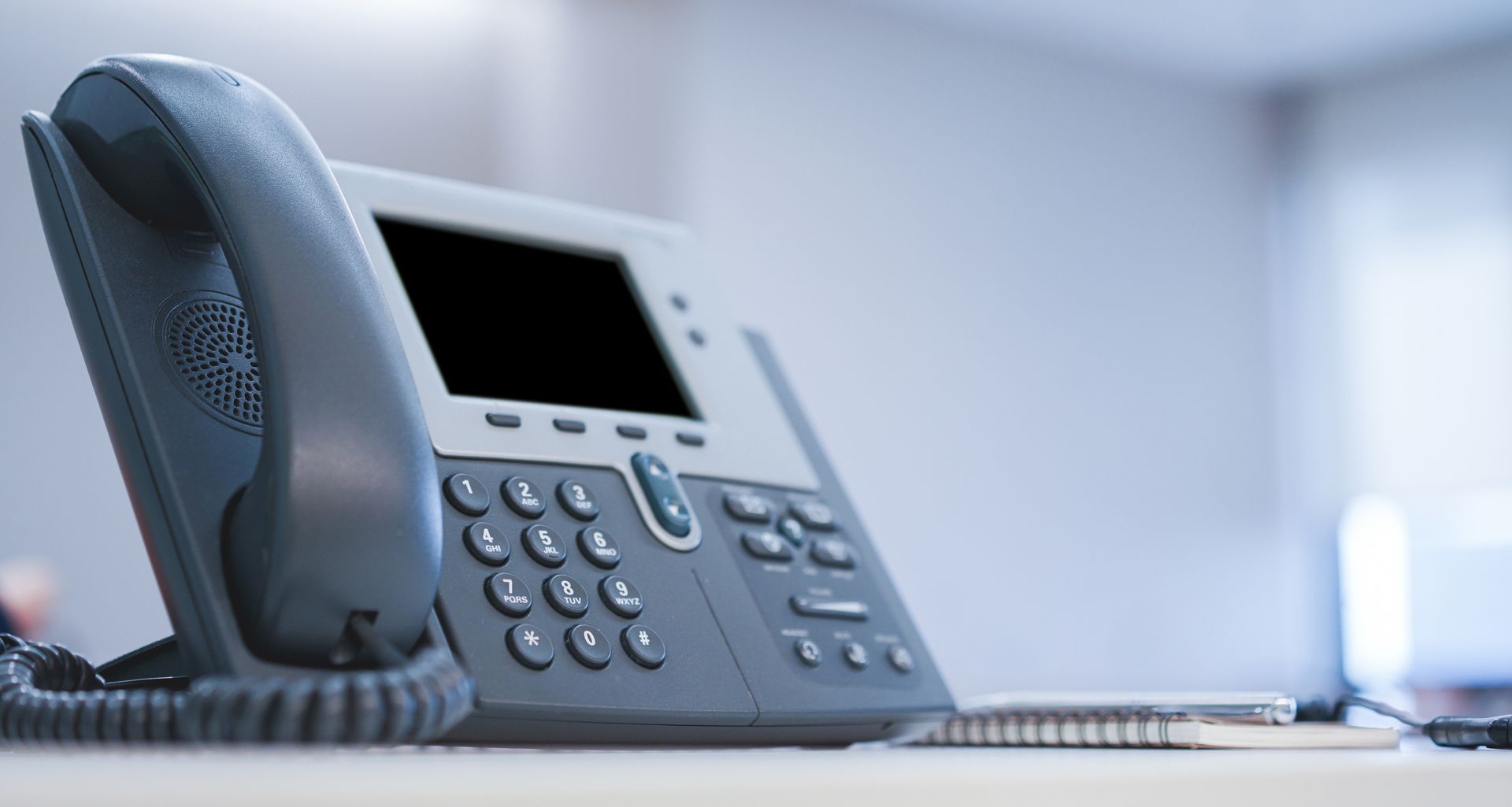 Office telephone with handset, keypad, and screen.