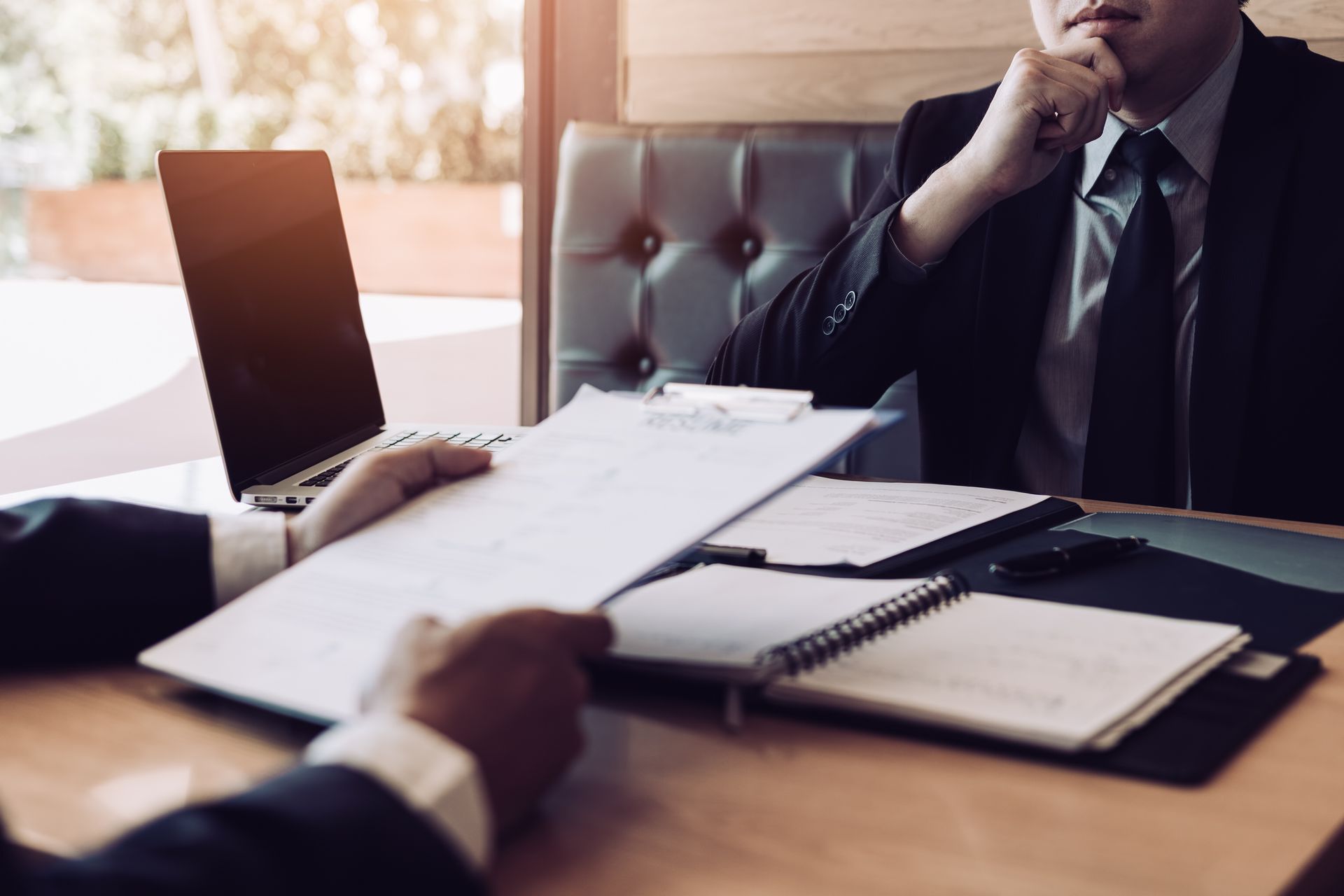 Two men in suits reviewing documents at a desk, possibly in an office setting.
