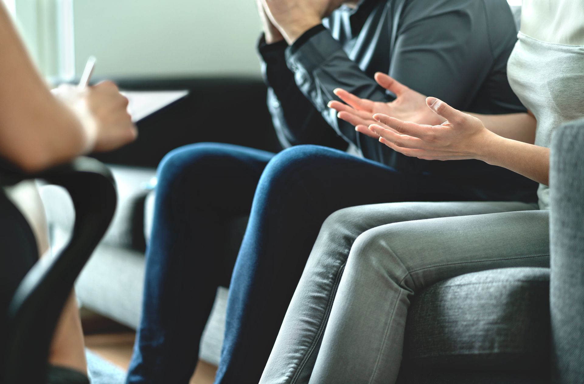 Couple in therapy session, one being comforted, hands gesturing, seated on a couch.