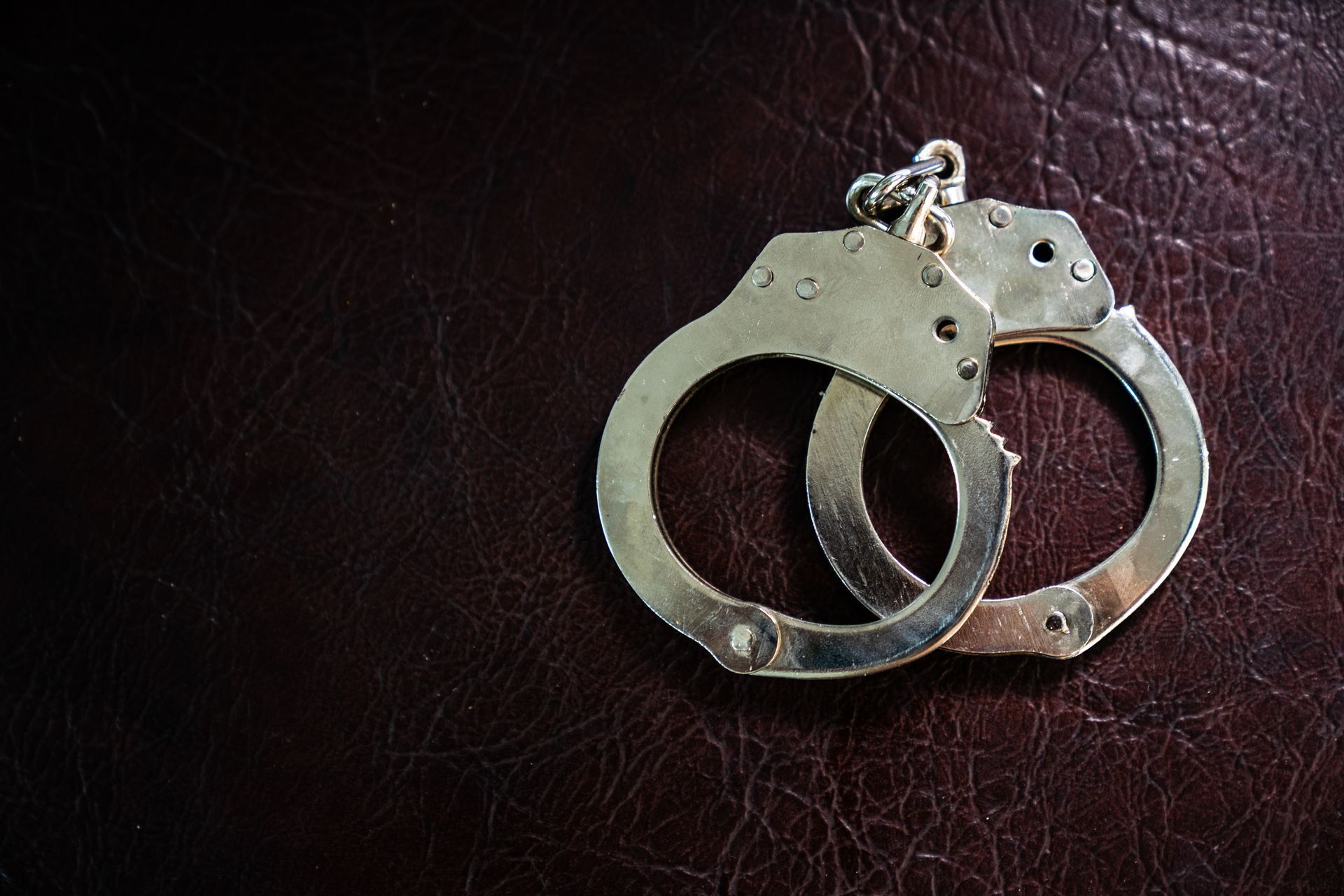Handcuffs on a dark brown leather surface.