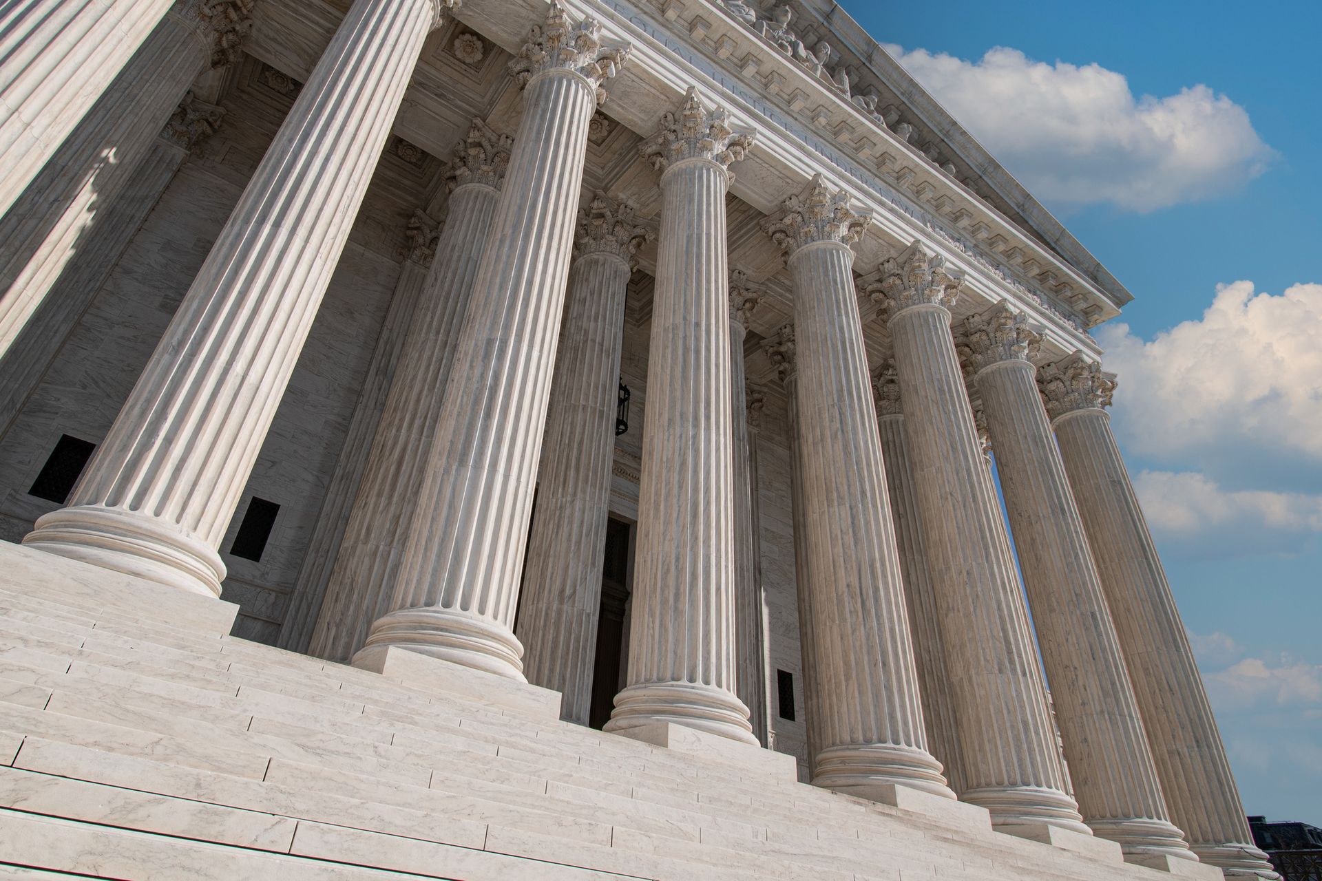 Exterior view of the U.S. Supreme Court building with columns, steps, and a blue sky with clouds.