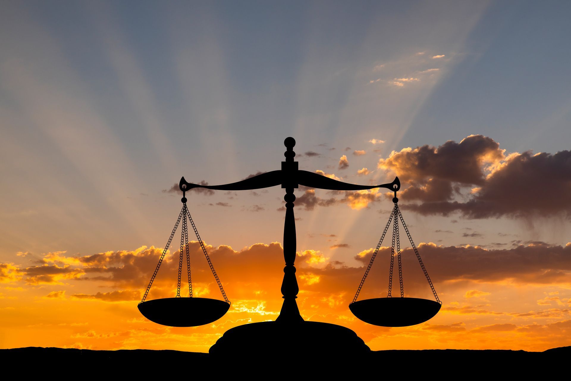 Silhouette of scales of justice against a fiery sunset, symbolizing fairness and law.