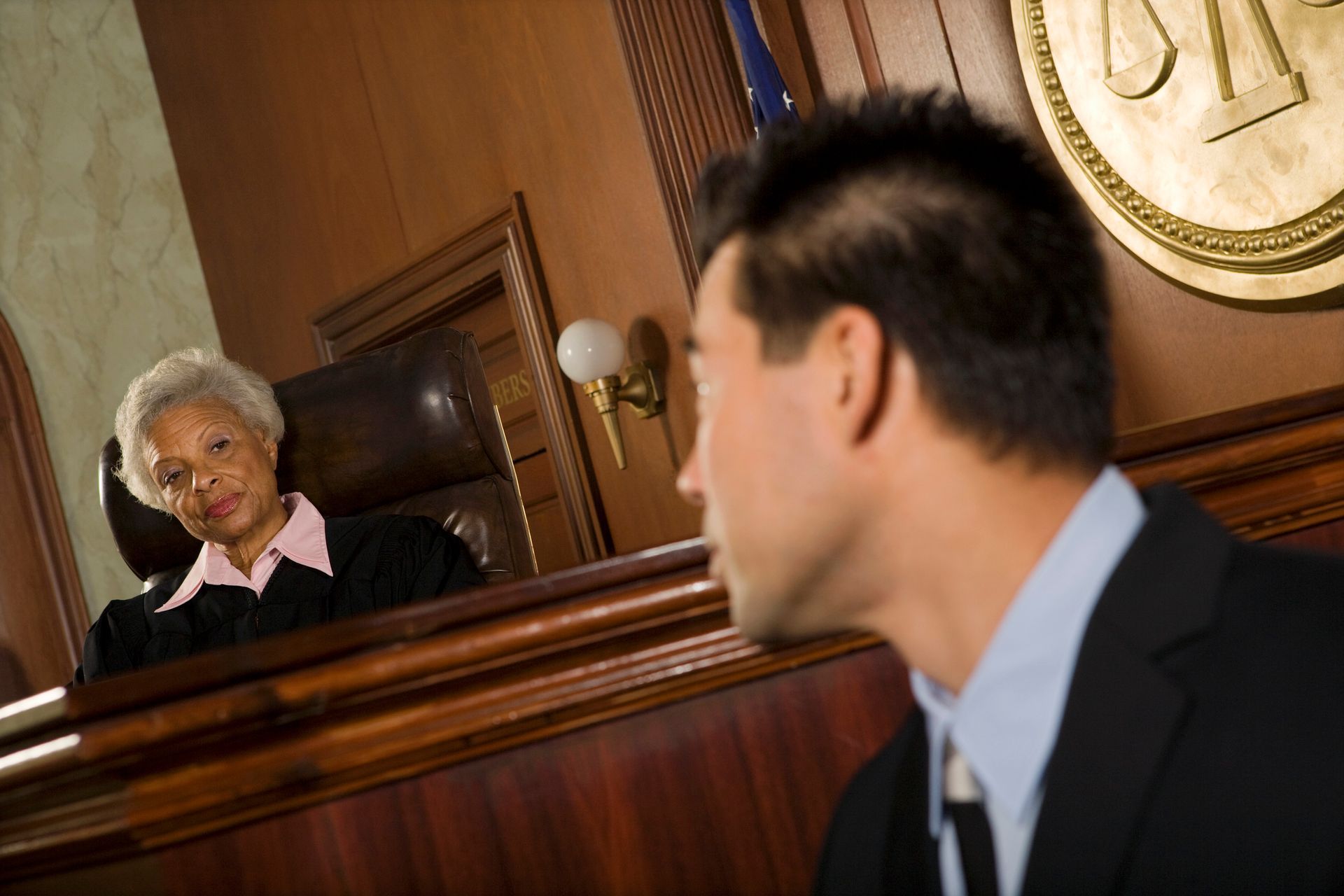 Judge in black robe seated, facing a man in a suit in a courtroom setting.