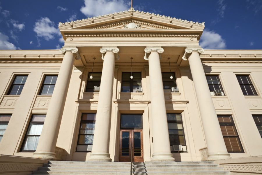 Beige courthouse with large columns, a blue sky, and a flag.