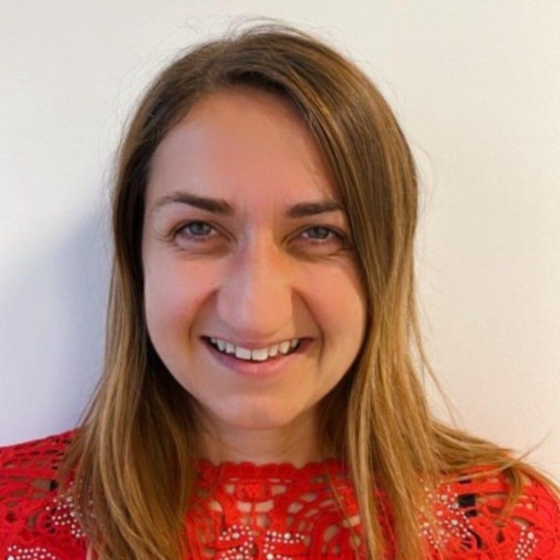 Woman with light brown hair, smiling, wearing a red lace top.