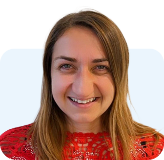 Woman with long brown hair smiles, wearing a red lace top, against a light blue background.