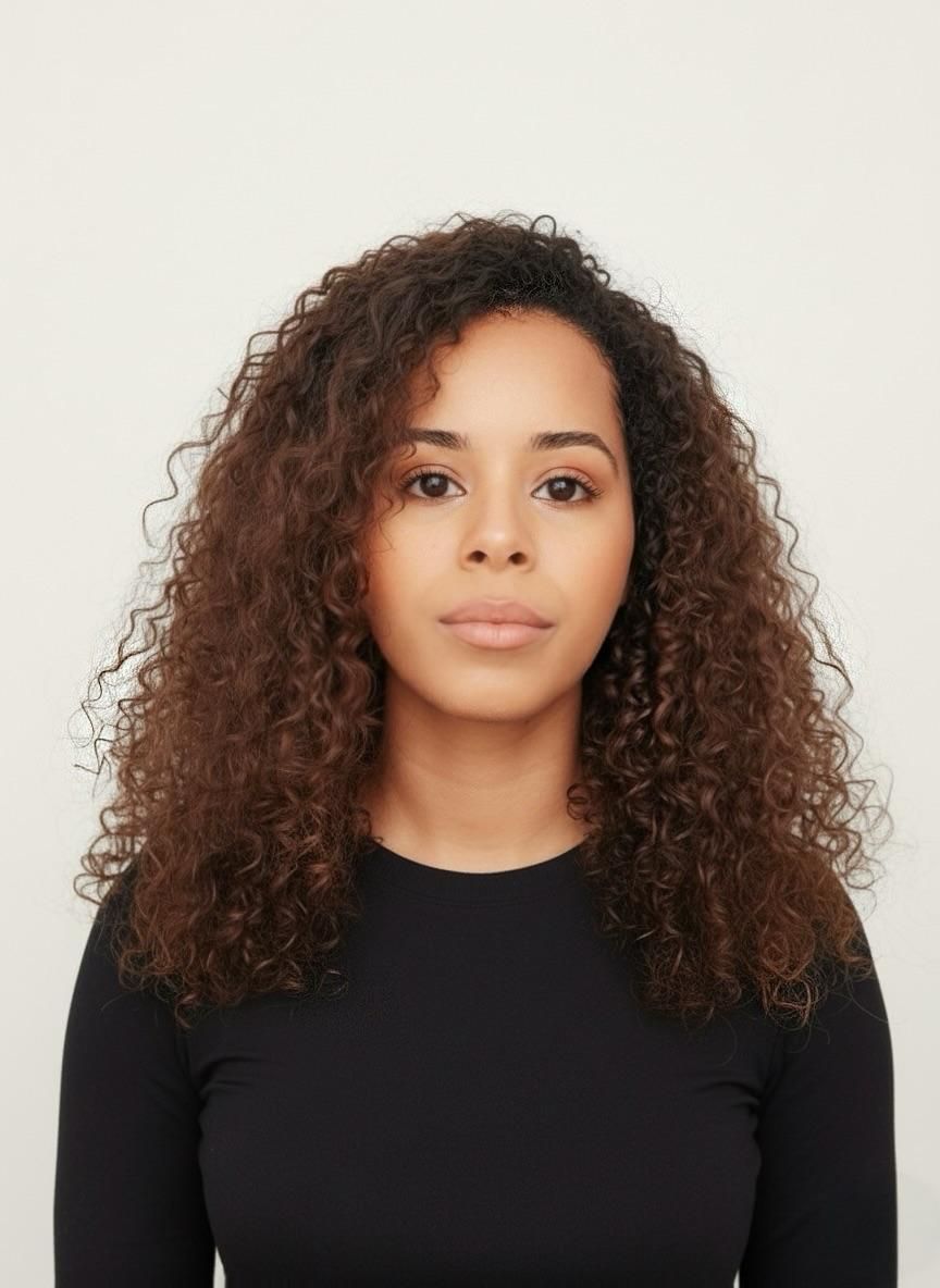 Woman with curly brown hair, wearing a black long-sleeved shirt, looking directly at the camera.